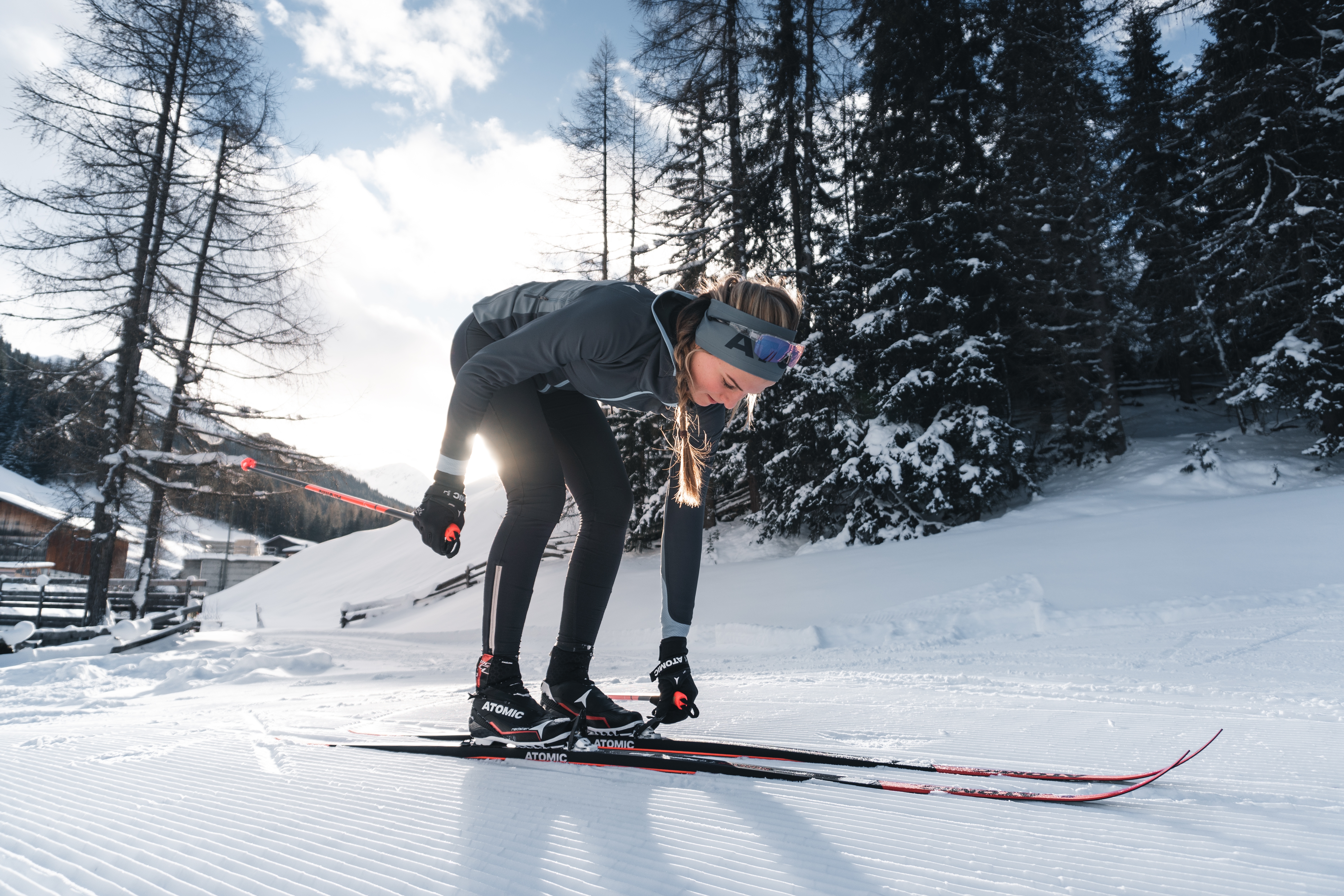 Une femme s'accroupi sur une piste de ski de fond afin de s'étirer.